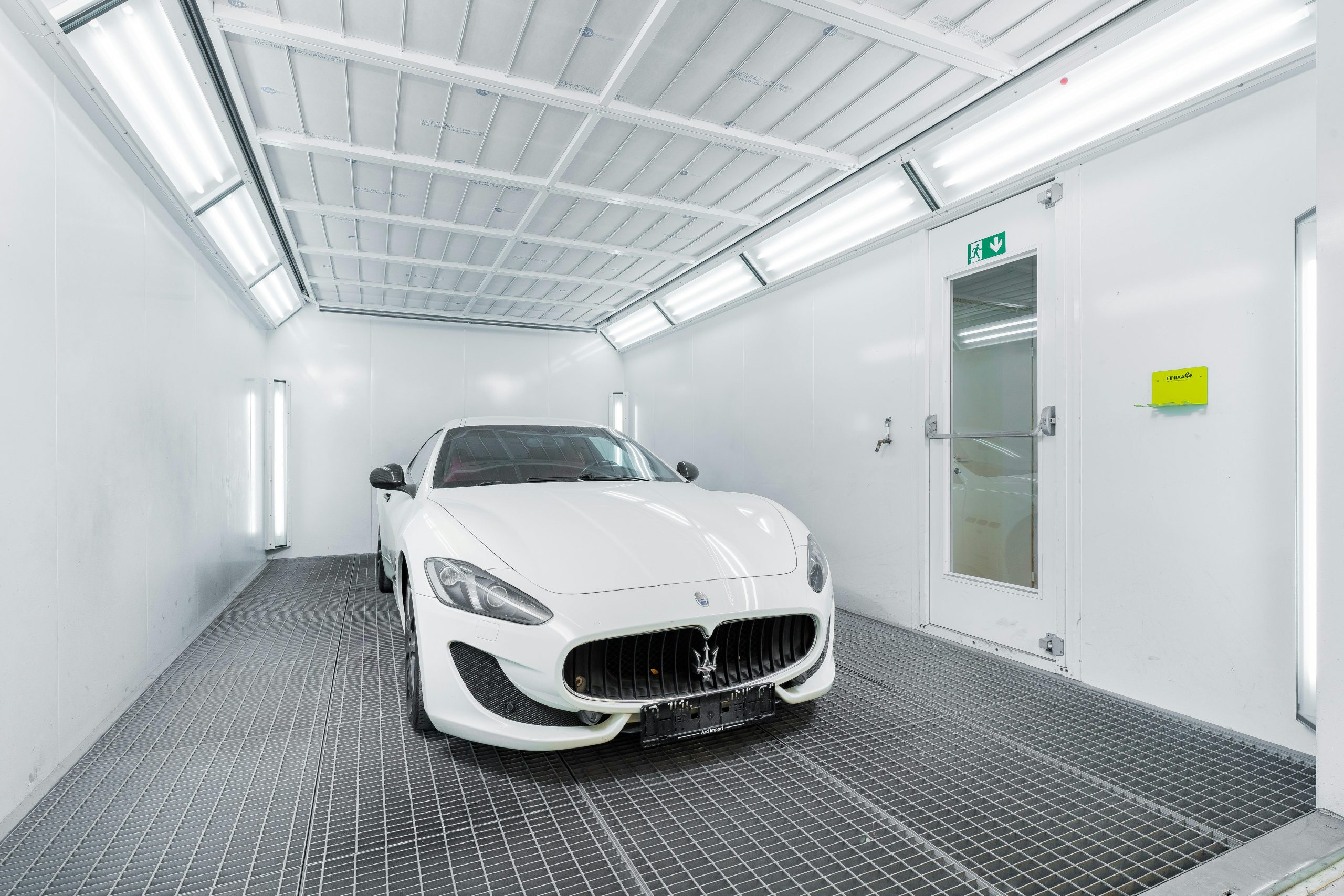 White luxury car inside a well-lit paint booth, showcasing sleek design and sophistication.